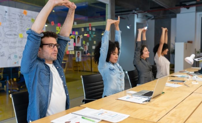 Prevenir: mejor que lamentar. En la imagen se observa a 3 ejecutivos haciendo ejercicios de estiramiento en su oficina.